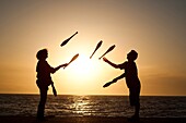Two people juggling with clubs at sunset on Aberystwyth promenade wales UK