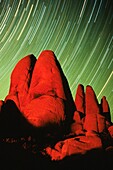 Large granite rocks lit by campfire with star trails whirling in the background at Joshua Tree National Park, California, USA