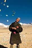 A Tibetan man throws paper wishes and prayers into the air in Tibet