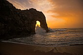 Durdle Door sun setting through arch during rough weather