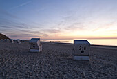 Roofed wicker beach chairs at beach in sunset, Sylt island, Schleswig-Holstein, Germany
