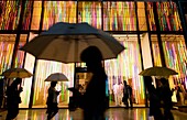 Exterior night view of Louis Vuitton store in rainy weather with people holding umbrellas in Tokyo Japan