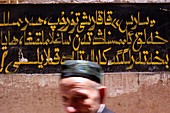 Muslim man walks past a sign with Arabic writing in the old town of Kashgar in Xinjiang Province of China