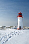 Lighthouse List West on snow covered dunes showing tracks of people leading to the lighthouse, with a bright blue sky at a sunny day, Sylt, Northfrisian Islands, Schleswig-Holstein, Northern Germany, Europe