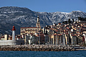 Colourful House Facades In The Old Town Of Menton And The Saint-Michel-Archange Basilica With Its Campanile In Front Of The Snow-Covered Mountains, Alpes-Maritimes (06), France