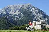 Woman riding a bike on Ennstal bicycle route with palace Trautenfels and Grimming in background, valley of Ennstal, Ennstal bicycle route, Styria, Austria