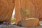 Woman sitting in front of red granite rock face, Spitzkoppe, Namibia