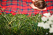 Young woman lying on red checked blanket on grass
