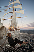 Junge Frau entspannt sich im Netz am Bugspriet vom Großsegler Kreuzfahrtschiff Star Flyer (Star Clippers Cruises) bei Sonnenuntergang, Pazifischer Ozean nahe Costa Rica, Mittelamerika, Amerika