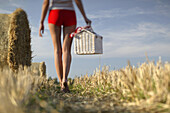Young woman with picnic basket walking through stubblefield, Upper Bavaria, Germany