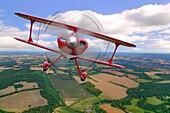A red stunt biplane in flight over rural countryside