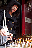 Oil lamps and butter lamps, woman lighting a candle, buddhist ritual, Luohan Temple, buddhist temple downtown, Chongqing, People's Republic of China