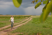 Radfahrerin auf einem Feldweg, Maisfeld im Hintergrund, bei Stolpe, Insel Usedom, Mecklenburg-Vorpommern, Deutschland