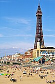 English seaside summer holiday People sunbathing on Blackpool Beach beneath Blackpool Tower, Lancashire, England