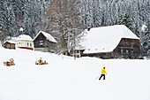 Cross-country skier passing old farmhouse, Hinterzarten, Black Forest, Baden-Wurttemberg, Germany