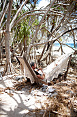 Gast in der Hängematte am Strand unter Pandanus Bäumen, Wilson Island Resort, Wilson Island, Teil des Capricornia Cays National Park, Great Barrier Reef Marine Park, UNESCO Weltnaturerbe, Queensland, Australien