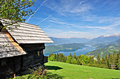 Old farmhouse on meadow high above lake Millstaetter See with snow covered mountains in the background, lake Millstaetter See, Carinthia, Austria, Europe