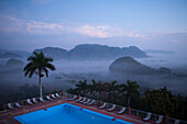 Swimming pool of Hotel Los Jazmines and fields in Vinales valley with steep-sided limestone mountains (mogotes) of Vinales National Park at dawn, Vinales, Pinar del Rio, Cuba