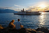 Youg couple watching a ferry at sunset on Lac Leman lake Geneva - Montraux Switzerland