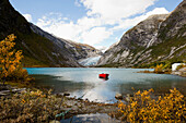 Blick auf Nigardsbreen, rotes Holzboot liegt im See vor der Gletscherzunge, Herbst, Jostedalen, Nigardsbreen, Jostedalsbreen Nationalpark, Sogn og Fjordane, Norwegen, Skandinavien, Europa