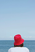 Woman wearing a red hut sitting at beach, List, Sylt, Schleswig-Holstein, Germany