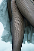Woman in fishnet stockings crossing legs, close-up, cropped view