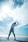 Person standing at the beach, arms raised, rear view, defocused