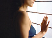 Woman standing next to window with hand against glass, cropped