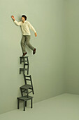 Man standing on top of stacked chairs and tables, one arm raised