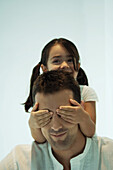Little girl covering father's eyes with her hands, smiling, laughing
