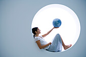 Young woman reclining on windowsill, holding globe