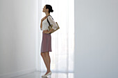 Woman standing beside window, looking up, side view