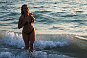 Woman running through surf at beach, laughing
