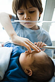 Young boy looking down at newborn sibling and touching its forehead