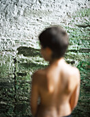 Shirtless boy near wall, rear view