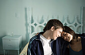 Young couple sitting on edge of bed with heads together
