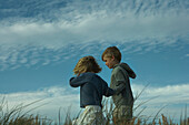 Boy and girl walking side by side through tall grass, holding hands