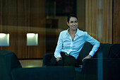 Businesswoman sitting in lobby, looking away, smiling