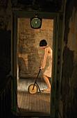 Woman standing on scooter on hardwood floor, seen through doorway