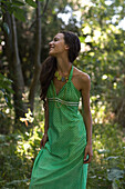 Young woman wearing sundress, standing in forest, looking away, three quarter length