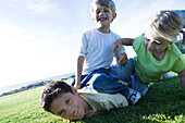 Three children wrestling on grass, smiling