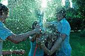 Young friends having water fight with garden hose