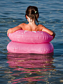 Young Girl Sitting in Pnk Floating Rings in Water, Rear View