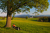 Hiker resting on a bench, St. Marinus pilgrimage church, Wilparting, Irschenberg, Wendelstein, Bavaria, Germany, Europe