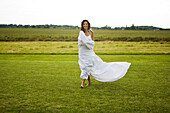 Young woman in a field, white sheet on her body, oudoors