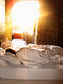 Person Sleeping in Hotel Bed With Sunlight Streaming Through Window