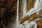 Mann steht auf Klippe im Wasserfall bei Ouzoud, Hoher Atlas, Marokko, Afrika