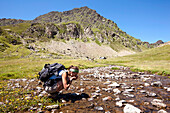 Female hiker drinking from a river near lake Lac Roumassot, Ossau Valley, French Pyrenees, Pyrenees-Atlantiques, Aquitaine, France