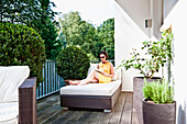Woman sitting on a lounger while using an iPad on a balcony, Hamburg, Germany