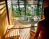 Man sitting in a sauna, woman standing outside on terrace,  Vigiljoch, Lana, Trentino-Alto Adige/Suedtirol, Italy